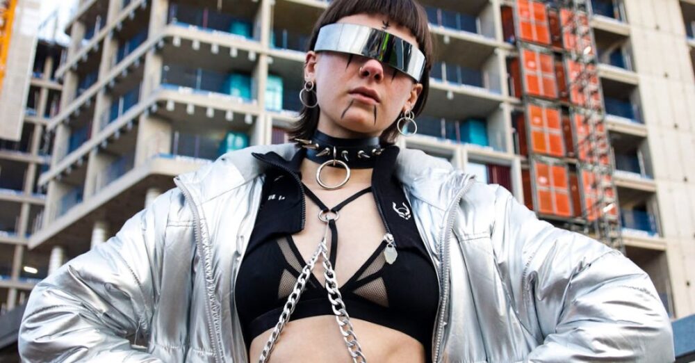 Sites - A woman in a silver jacket and sunglasses standing in front of a construction site