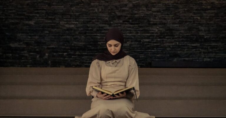 Sites - A woman in a hijab sitting on the floor reading a book